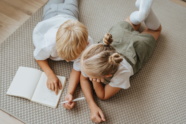 Kids lying on the carpet and writing in a notebook