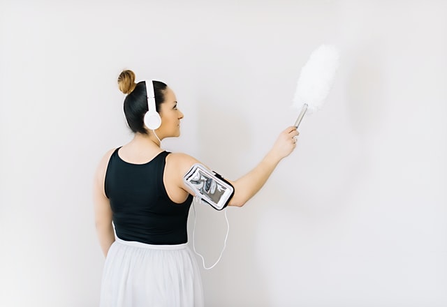 8 Places You're Probably Forgetting to Clean 1 Woman wearing a headset dusting a wall which is one of the places you're probably forgetting to clean